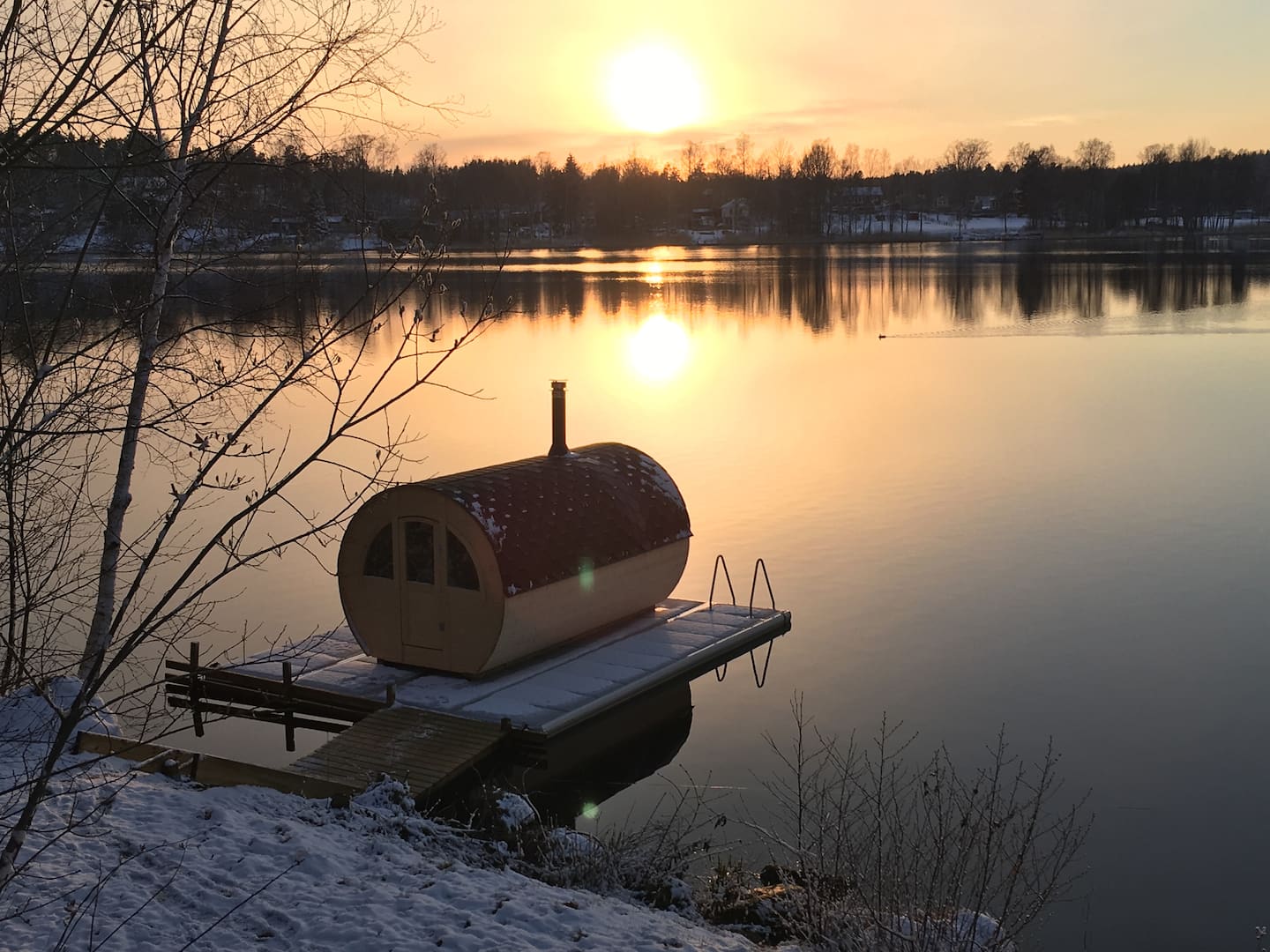 Bastun vid stranden en vinterkväll med snö och solnedgång över Borsöknasjön
